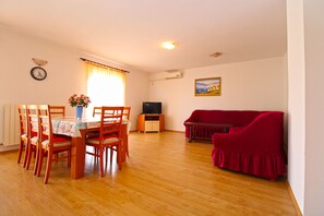A living room with a dining table, chairs, a red sofa, a television, and a painting on the wall.