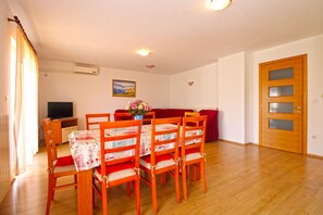 A dining area with a table set for four, wooden chairs, a red sofa, and a television in the background.