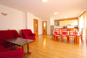 A living room with a wooden table and red chairs, a kitchen with wooden cabinets, and a dining area with a table and chairs.
