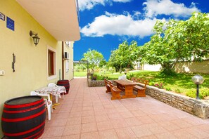 Eine Terrasse mit Holztisch und -stühlen, einem Fass und einem weißen Stuhl.