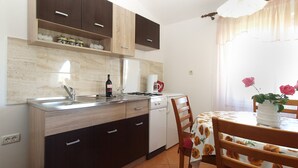 A compact kitchen with dark cabinets, a white countertop, and a dining area with a floral tablecloth. - Apartment 777/1814 (Istria - Fažana), 500m from the beach (Fažana)