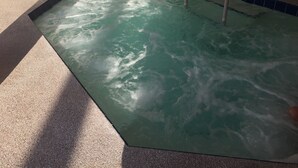 Un jacuzzi con borde de azulejos azules y una escalera de metal.
