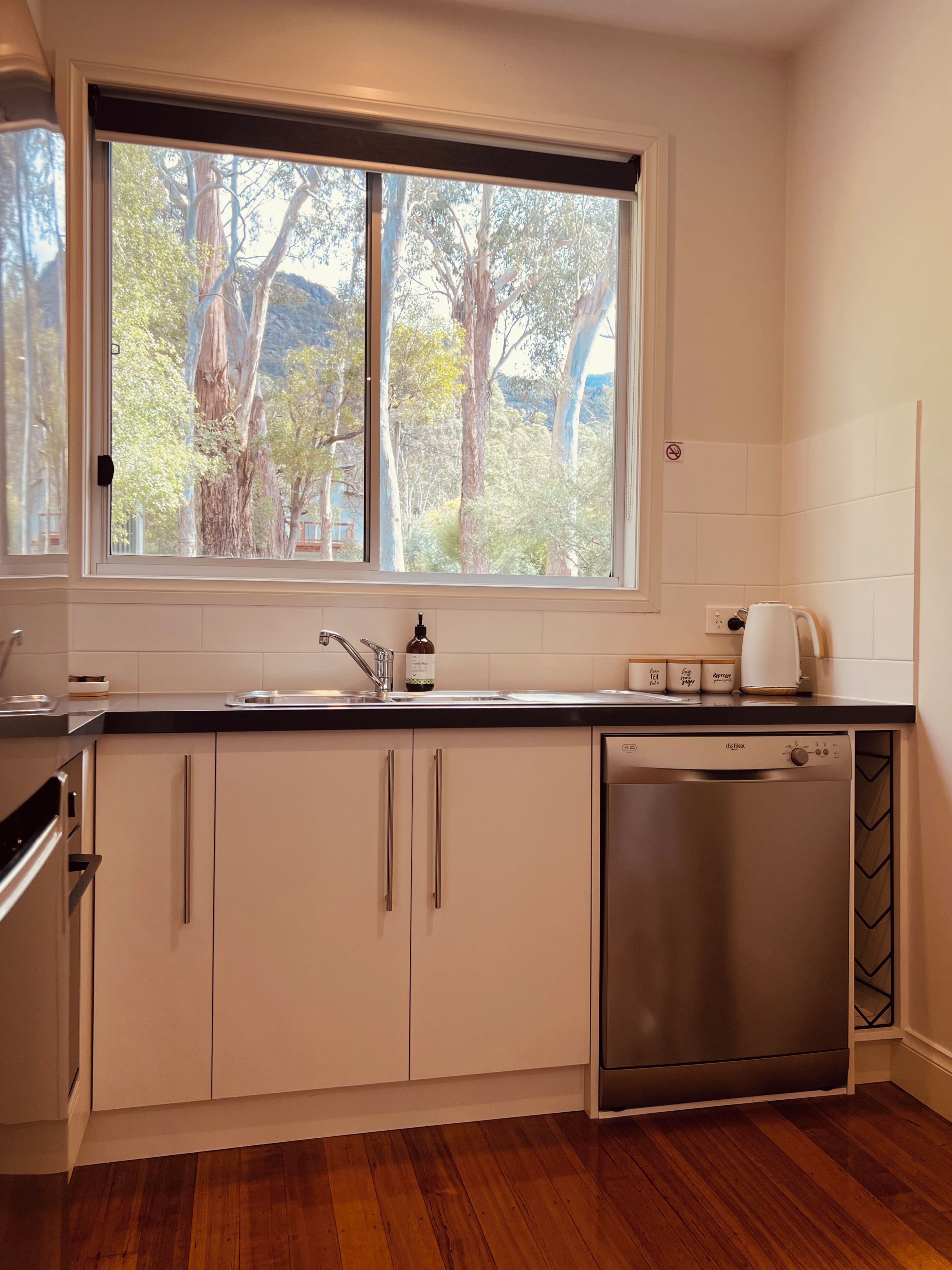 A modern kitchen with a dishwasher, a sink, and a window overlooking a garden.