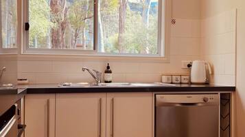 A modern kitchen with a dishwasher, a sink, and a window overlooking a garden.
