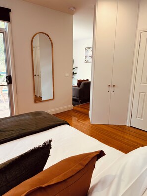 A bedroom with a bed, a mirror, a wardrobe, and a door leading to another room.
