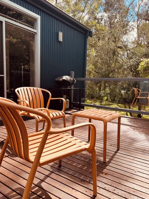 A wooden deck with outdoor furniture, a barbecue grill, and a blue building with a sliding glass door.