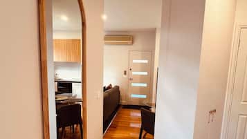 A hallway with wooden flooring, a large mirror, a dining area with a table and chairs, and a kitchen in the background.