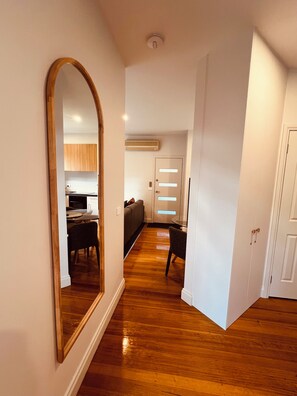 A hallway with wooden flooring, a large mirror, a dining area with a table and chairs, and a kitchen in the background. - Manuka Retreat, Free unlimited WIFI.... (Halls Gap)