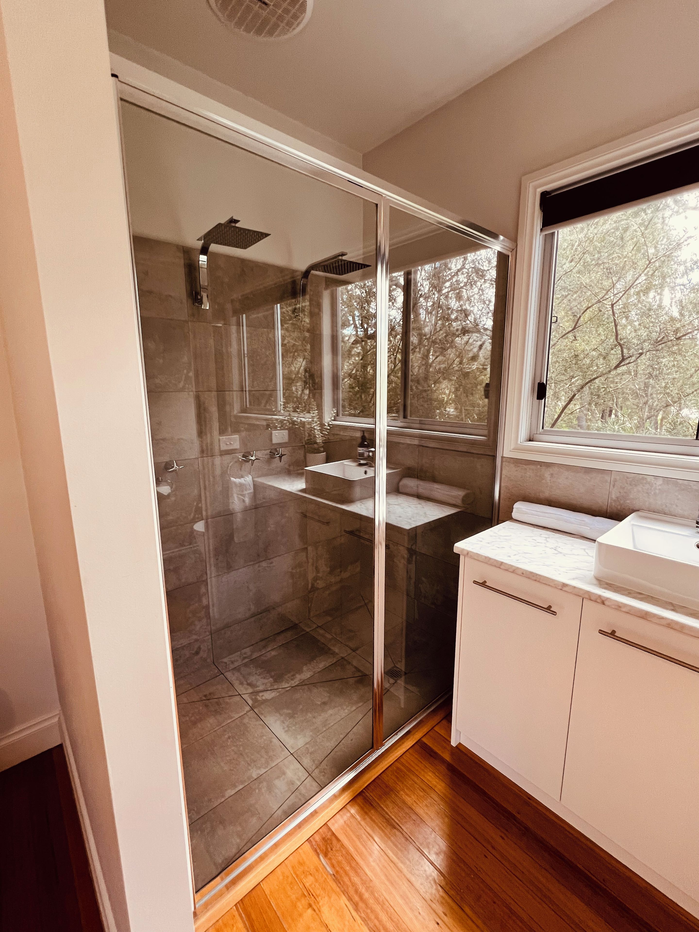 Een moderne badkamer met een douchecabine van glas, een wastafel en een raam met uitzicht op bomen.