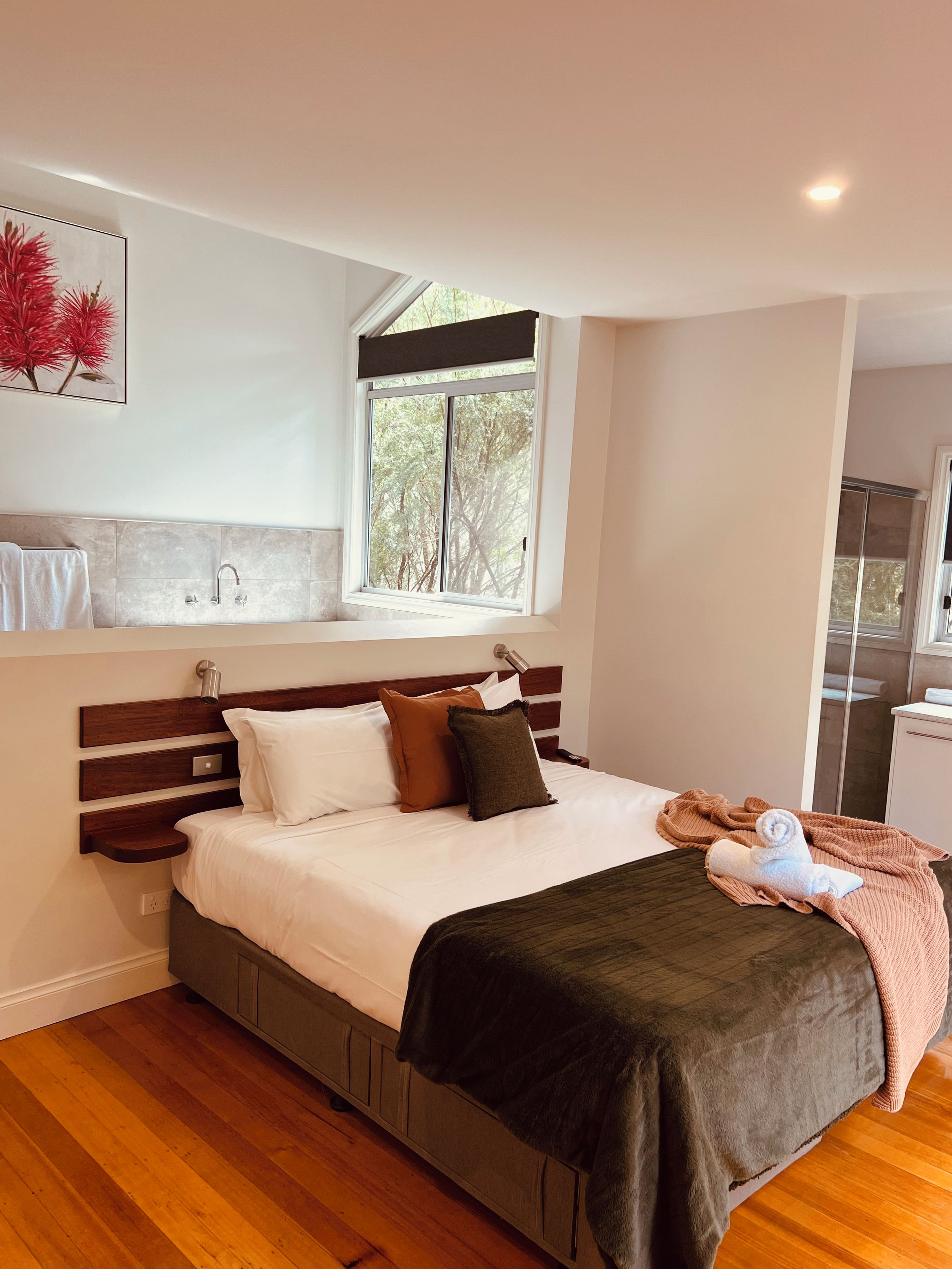 A modern bedroom with a wooden headboard, a large window, and a view of trees outside.