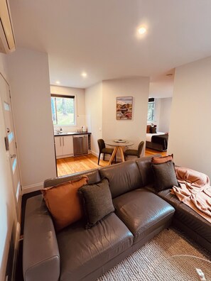 A modern living room with a leather sofa, a dining table, and a kitchen in the background.