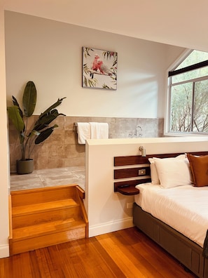A bedroom with a bed, a nightstand, a window, a painting, and a staircase leading to a bathroom. - Manuka Retreat, Free unlimited WIFI.... (Halls Gap)