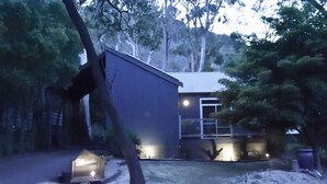 A small, single-story building with a sloped roof, surrounded by trees and a grassy yard. - Manuka Retreat, Free unlimited WIFI.... (Halls Gap)