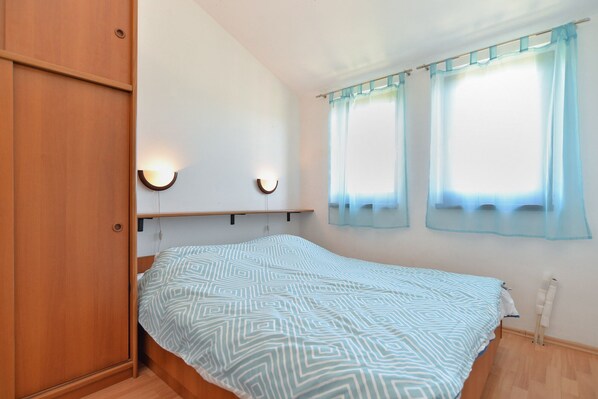 A bedroom with a bed, wooden wardrobe, two wall-mounted lights, and a window with sheer curtains.