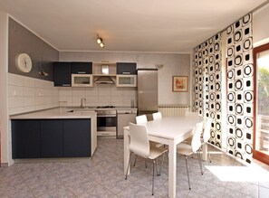 Une cuisine moderne dotée d’un îlot central, d’appareils électroménagers intégrés et d’un coin repas avec une table et des chaises blanches.