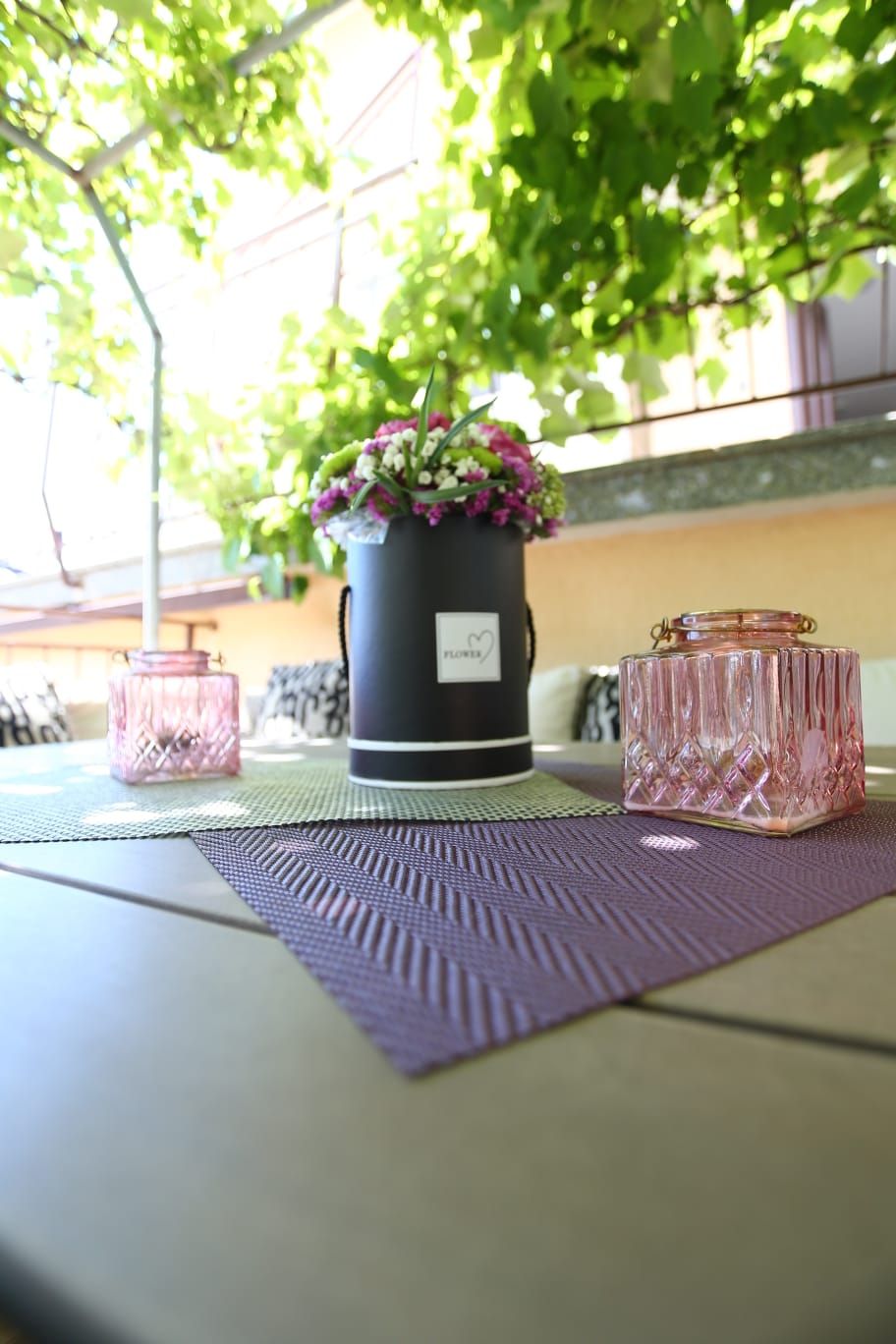 Une table ornée d’une plante en pot, de deux photophores en verre et d’un set de table en fibres tressées.