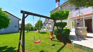 A swing set in a well-maintained garden with a stone building in the background. - Apartment 810/1888 (Istria - Medulin), 600m from the beach (Medulin)