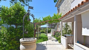 A pathway leading to a building with a stone barrel, a pergola with vines, and a street sign indicating the year 2007. - Apartment 810/1888 (Istria - Medulin), 600m from the beach (Medulin)