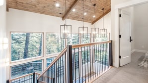 Un escalier avec une rampe en bois menant à un balcon doté de grandes fenêtres donnant sur une forêt.