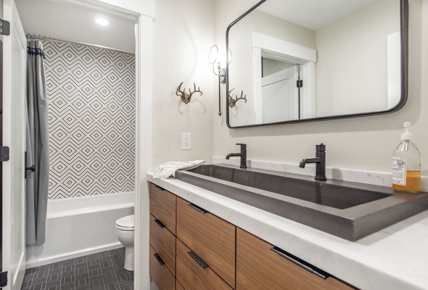 A bathroom with a double sink, wooden cabinets, a mirror, and a shower area.