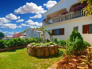 A building with a stone fountain, lush garden, and a balcony with potted plants.