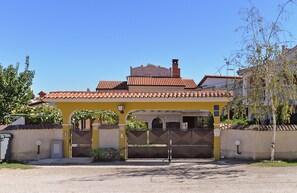 A yellow building with a tiled roof, a gated entrance, and a clear sky.