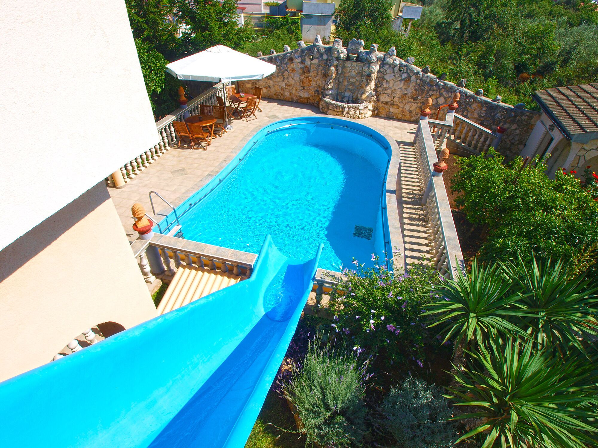 A swimming pool with a slide, surrounded by stone walls and greenery.