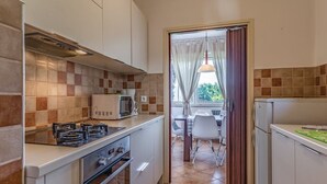 A compact kitchen with a gas stove, microwave, and oven. A dining area with a table and chairs is visible through an open door. - Apartment 812/1899 (Istria - Medulin), 300m from the beach (Medulin)