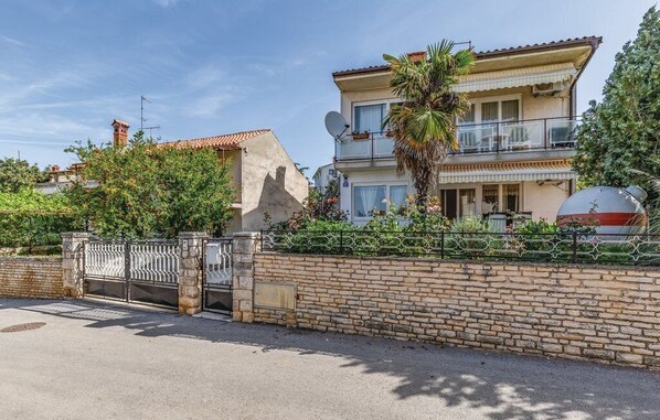 A two-story house with a balcony, a satellite dish, and a stone wall.