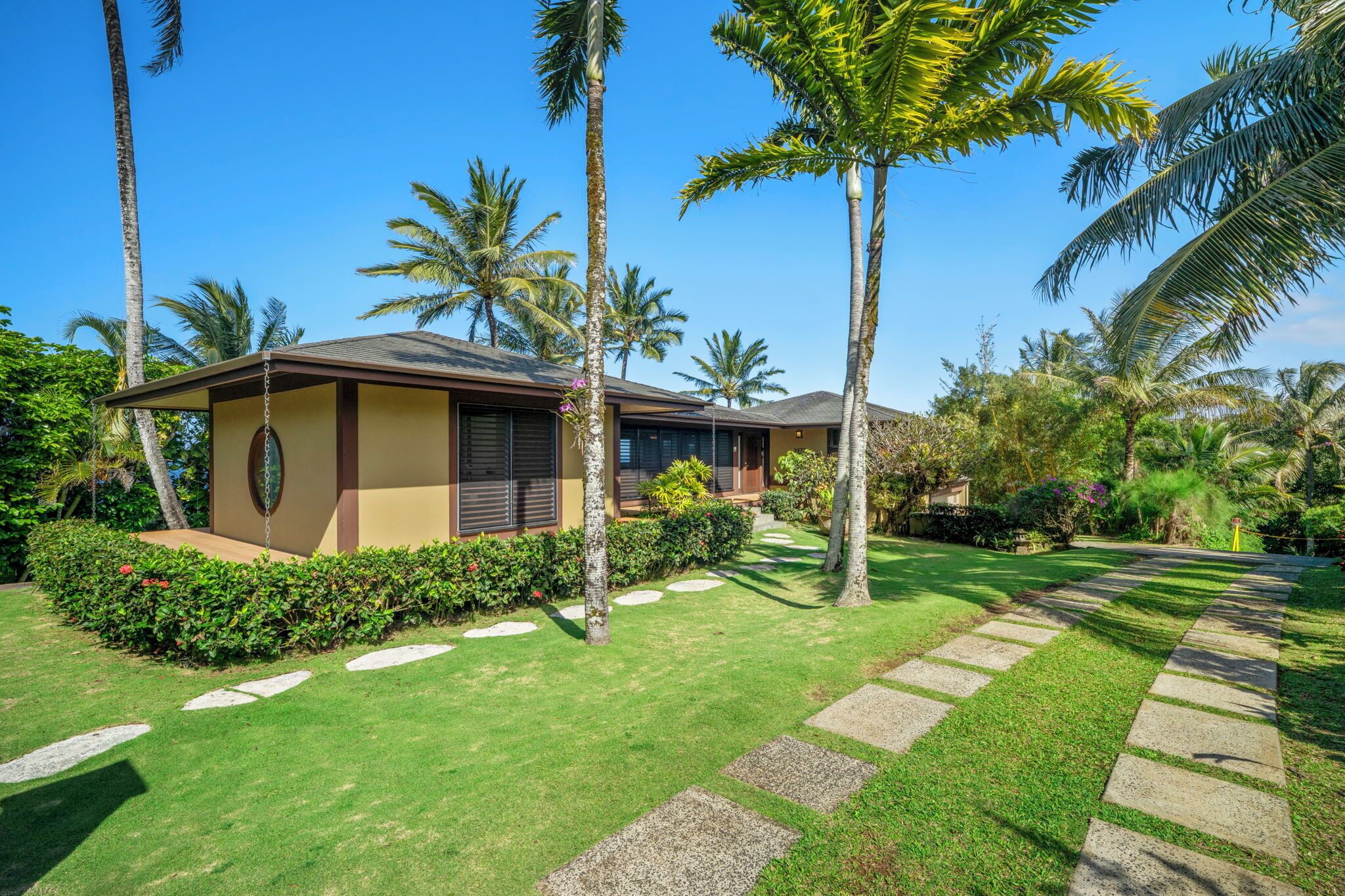 A modern house with a well-maintained lawn, palm trees, and a clear blue sky.