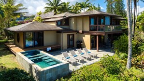 Une maison à deux étages dotée d’une piscine, d’un espace extérieur aménagé et entourée d’une végétation tropicale luxuriante.