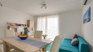 A modern living room with a wooden dining table, a teal sofa, and a kitchen area with a built-in shelf. - Apartment 813/1901 (Istria - Medulin), 90m from the beach (Medulin)