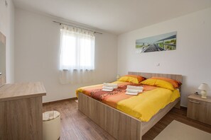 A bedroom with a wooden bed, a bedside table, a nightstand, a window with sheer curtains, and a painting on the wall. - Apartment 813/1901 (Istria - Medulin), 90m from the beach (Medulin)