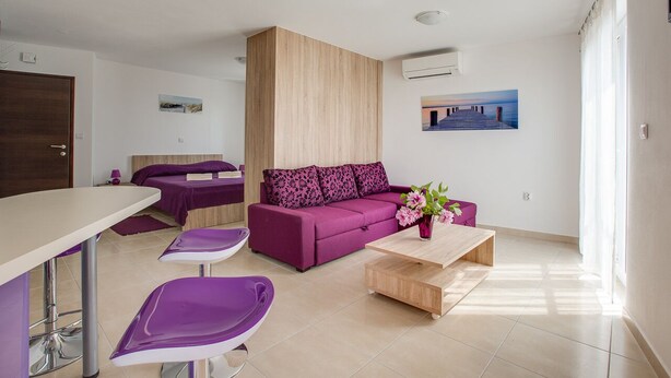 A modern living room with a purple sofa, a wooden coffee table, and a dining area with a white table and purple chairs. - Apartment 813/1902 (Istria - Medulin), 90m from the beach (Medulin)
