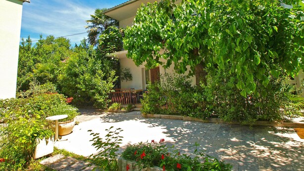 Une cour avec un bâtiment blanc, une végétation luxuriante et un chemin pavé de pierres.