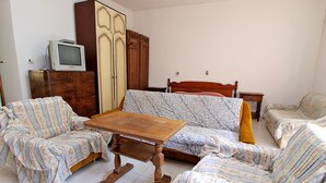 Un salon comprenant un canapé, deux fauteuils, une table basse en bois, un téléviseur et une armoire.