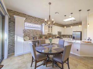 A modern kitchen with white cabinets, a central island, and a dining area with a round table and chairs.