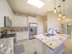 A modern kitchen with white cabinets, a granite countertop, a stainless steel refrigerator, and pendant lighting.