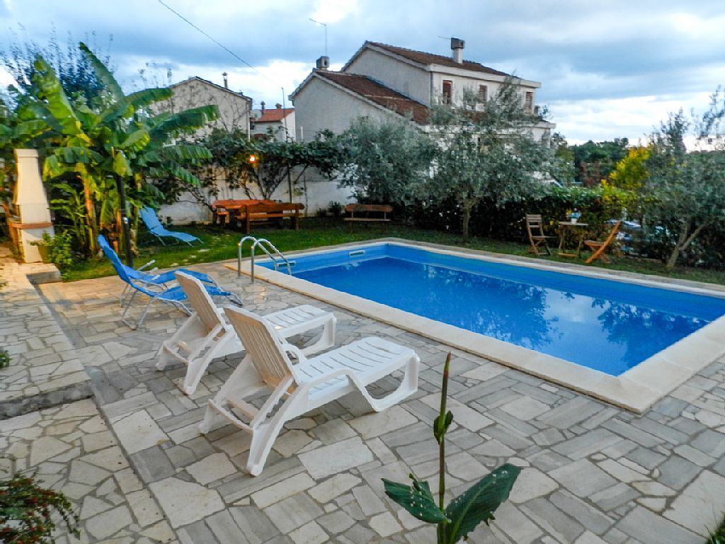 A rectangular swimming pool with a stone patio, surrounded by lounge chairs and greenery.