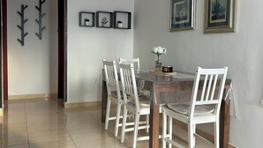 A dining area with a wooden table and white chairs, a chandelier, framed pictures on the wall, and a tiled floor. - Apartment 821/1924 (Istria - Pula), 2800m from the beach (Pula)