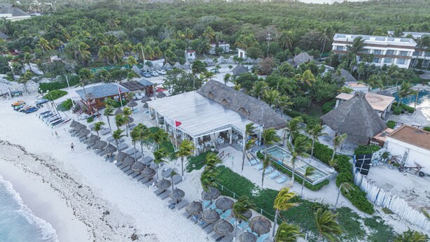 Vista aérea de un complejo turístico en la playa con piscina, sillas de descanso y palmeras.