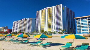 A beachfront hotel with multiple high-rise buildings, beach umbrellas, and sun loungers. - Good Times and Tan Lines! (Daytona Beach)
