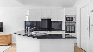 Une cuisine moderne avec des meubles blancs, un plan de travail noir, des appareils en acier inoxydable et un buffet en bois.