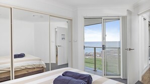 A bedroom with a bed, a large sliding glass door to a balcony, and a view of the sea. - Absolute Waterfront Anna Bay (Anna Bay)