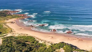 An aerial view of a coastal area with a sandy beach, rocky outcrops, and green vegetation. - Absolute Waterfront Anna Bay (Anna Bay)