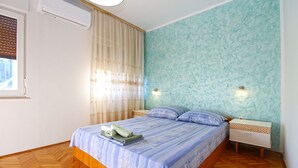 A bedroom with a bed, wooden floor, a window with blinds, and a wall-mounted light fixture. - Apartment 826/1935 (Istria - Pula), 75m from the beach (Pula)