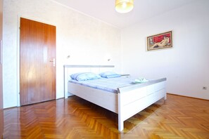 Une chambre avec un plancher en bois, un lit avec un cadre blanc et une porte.