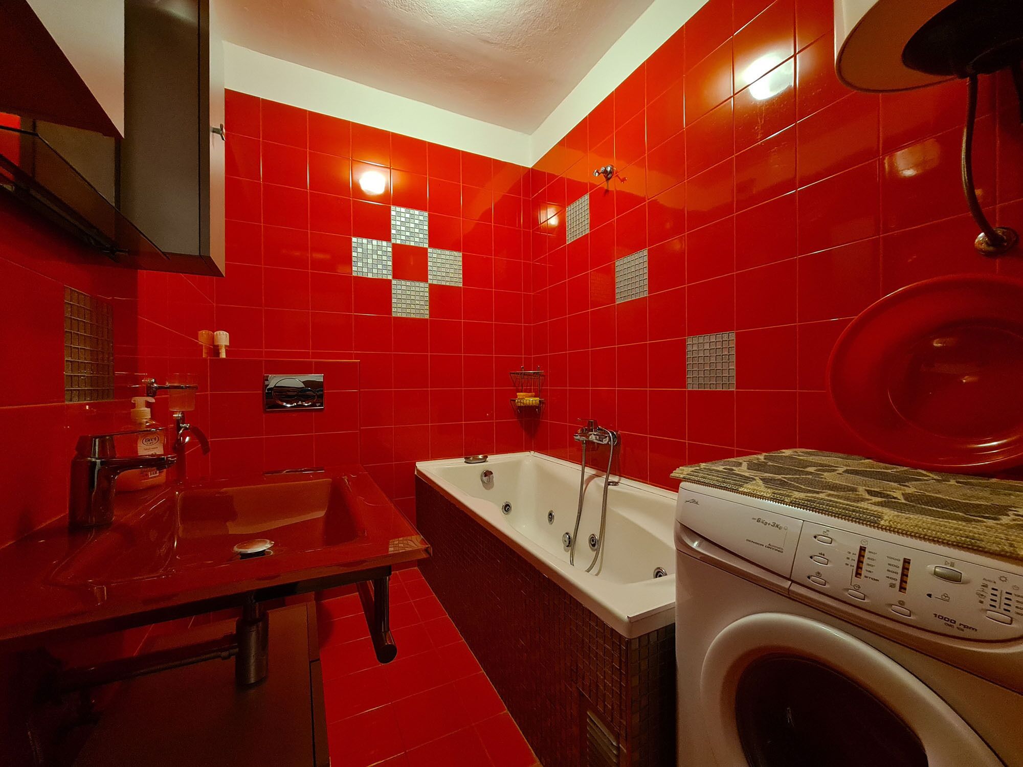 Une salle de bain moderne avec des carreaux rouges, une baignoire, un lavabo et un lave-linge.