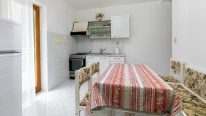 A compact kitchen with white cabinets, a stove, and a dining table with a patterned tablecloth. - Studio apartment 828/1937 (Istria - Rabac), 700m from the beach (Rabac)