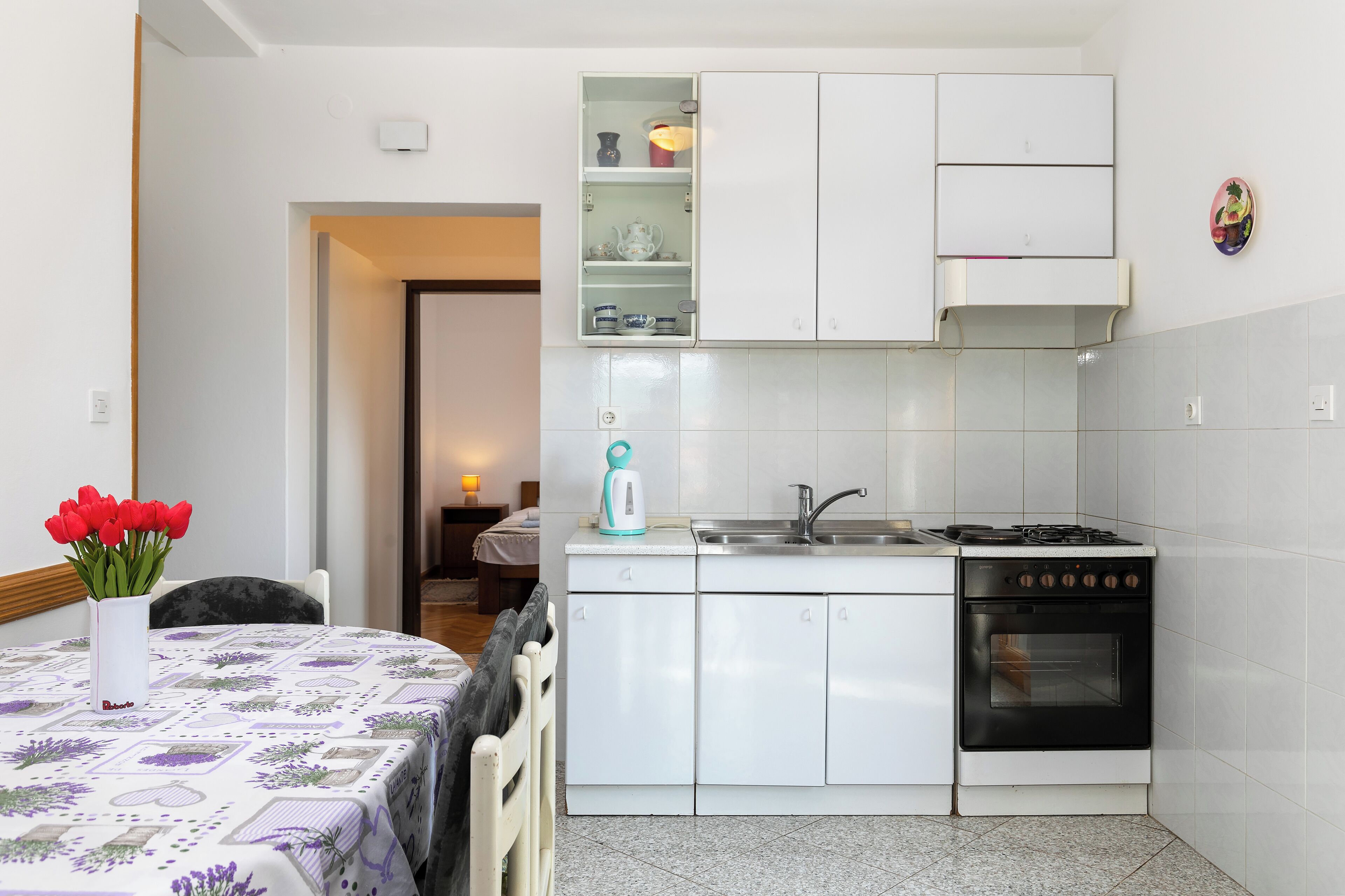 A kitchen with white cabinets, a stove, a sink, and a small shelf with kitchenware.